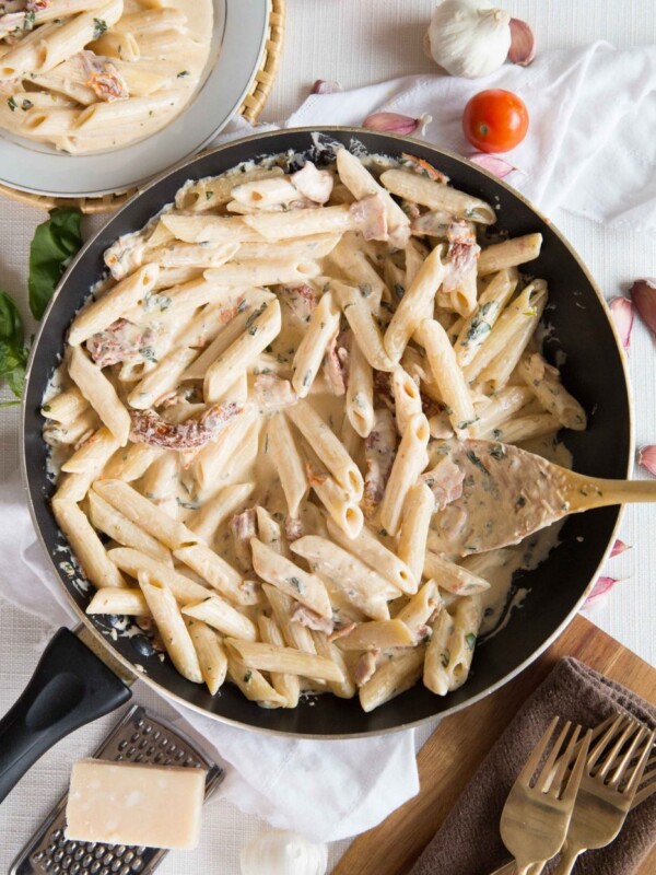 overhead shot of pasta in skillet surround by forks, garlic, parmesan and basil