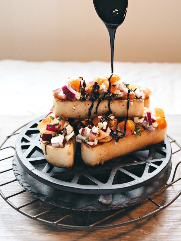 spoon dripping over balsamic glaze on to stack of bruschetta