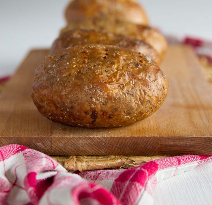 golden baked potato fresh out the oven on wooden board with more lined up blurred in the background