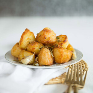 goose fat roast potatoes stacked on small white plate with gold forks in front on white cloth