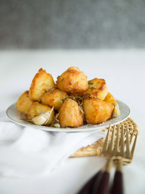 goose fat roast potatoes stacked on small white plate with gold forks in front on white cloth