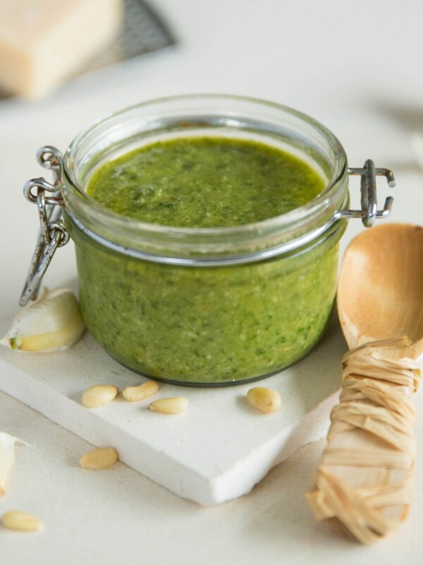 basil pesto in glass pot with serving spoon on white slate