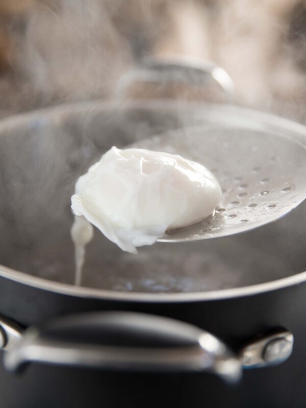 poached egg on a ladle above steaming pot of water