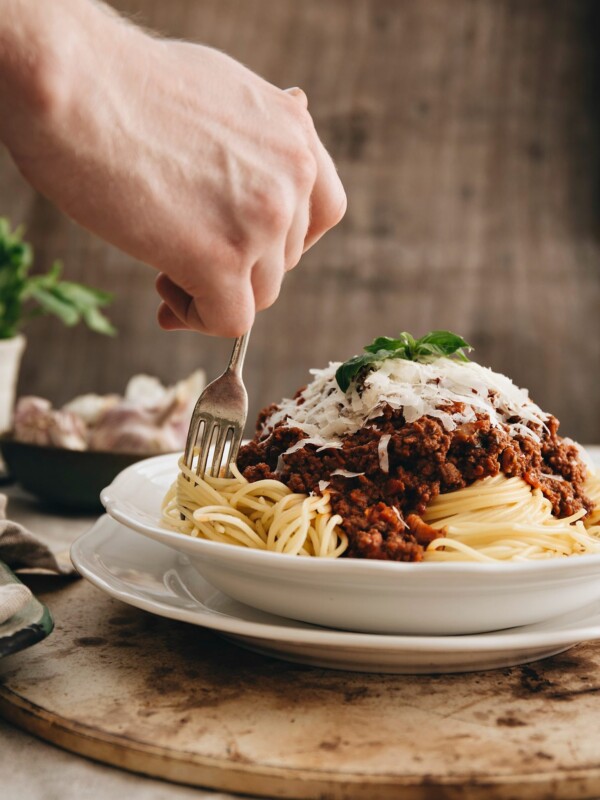 twisting fork into spaghetti bolognese in white bowl