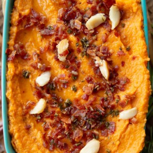 overhead shot of mash in baking dish garnished with bacon, rosemary and roasted garlic