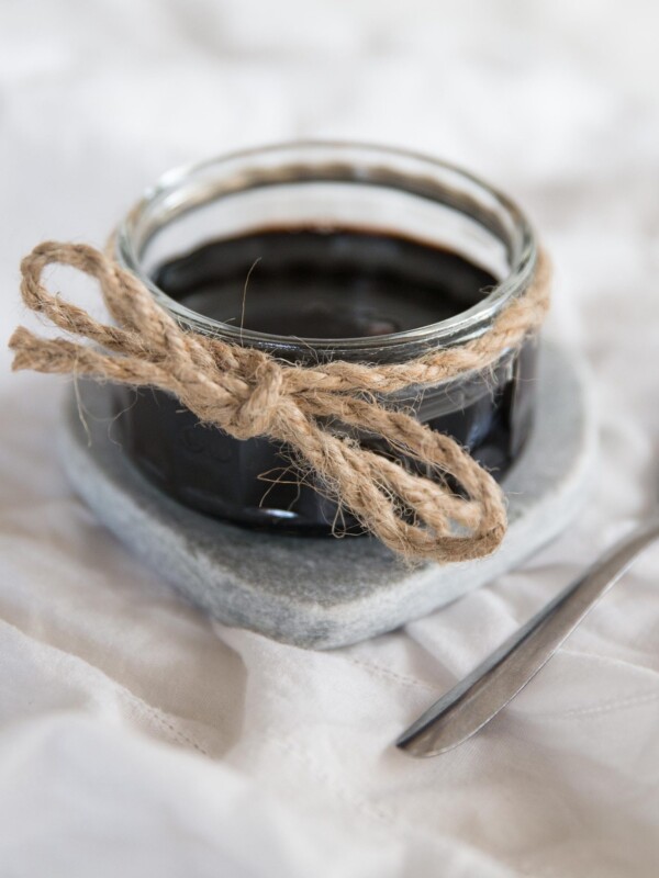 Homemade Balsamic Glaze in a glass jar on white sheet with tsp