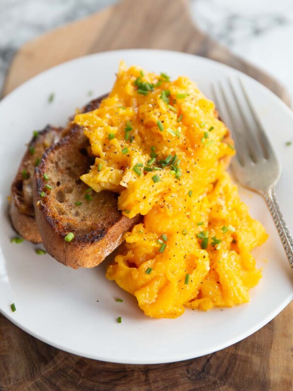 scrambled eggs served on two small slices of toast on white plate with silver fork