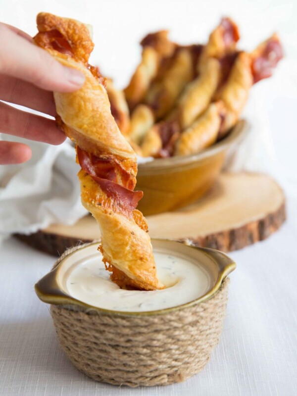 dunking cheese twist into small pot of sour cream dip with bowl of twists blurred in background