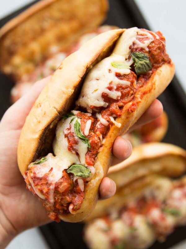 closeup shot of a hand holding meatball sub with melted cheese and 3 subs in the background