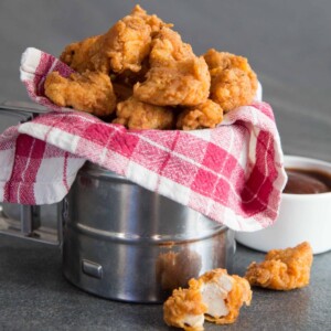 Popcorn Chicken in metal tub wrapped in tartan cloth with BBQ sauce in the background