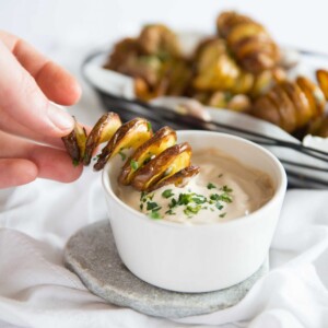 hand dipping tornado fry into small white pot of dip