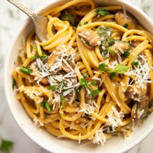 overhead shot of marmite pasta in small white bowl with silver fork on marble background