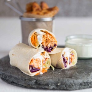 3 wraps stacked on one another with wedges and blue cheese dip blurred in background