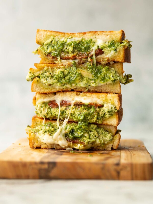 4 sandwich halves stacked on each other on wooden board showing chicken pesto filling