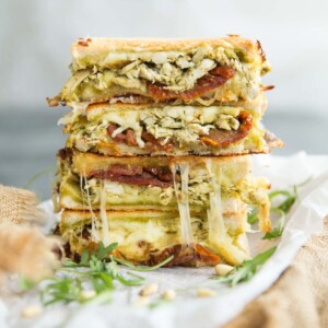 2 sandwiches stacked on each other garnished with arugula and pine nuts