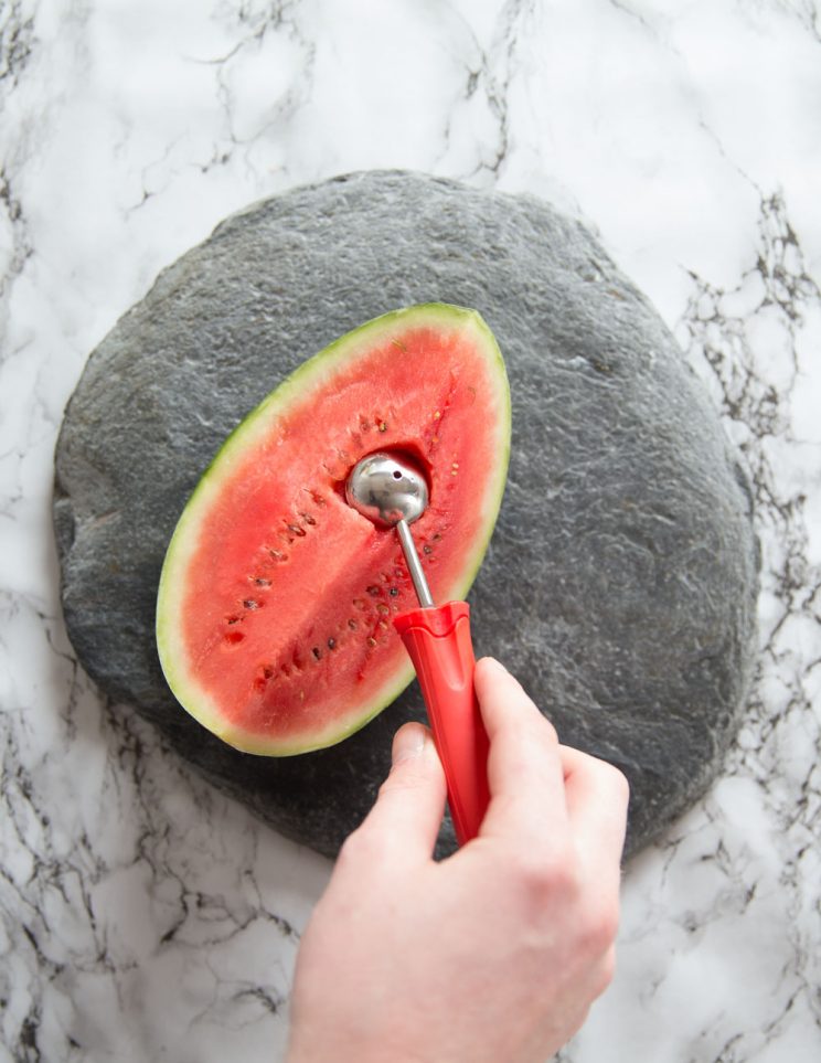 hand using melon baller to cut into 1/4 whole watermelon