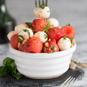 silver fork digging into small white pot of watermelon mozzarella salad