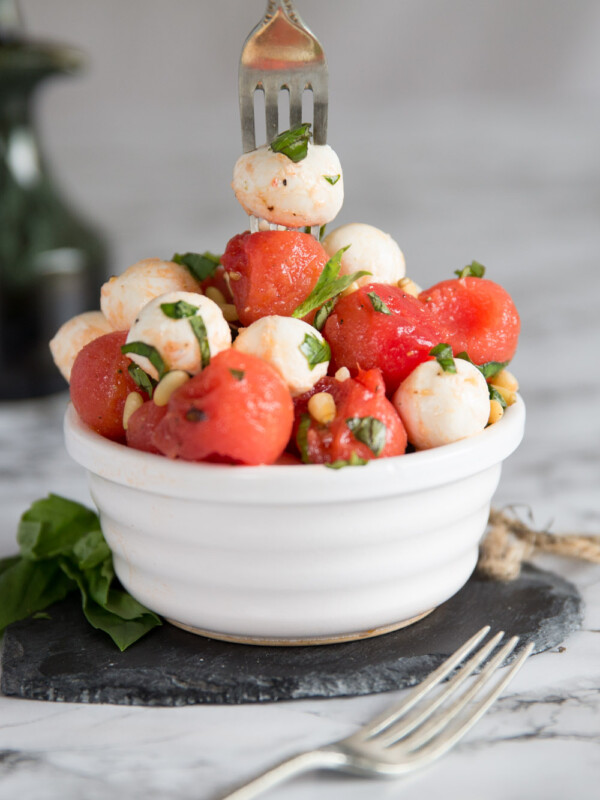 silver fork digging into small white pot of watermelon mozzarella salad