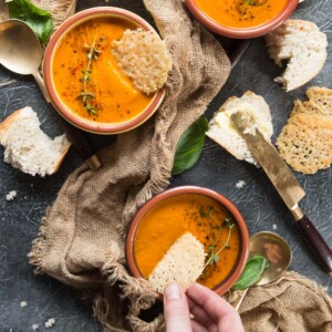 overhead shot of soup bowls with hand dunking parmesan chip into one