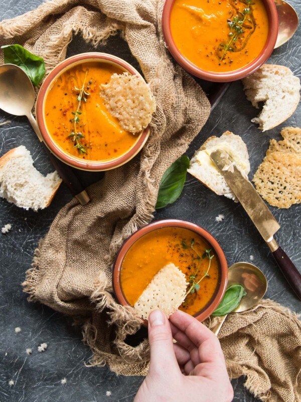 overhead shot of soup bowls with hand dunking parmesan chip into one