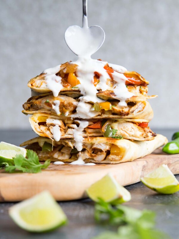 quesadillas stacked on each other with heart shaped spoon pouring over sour cream