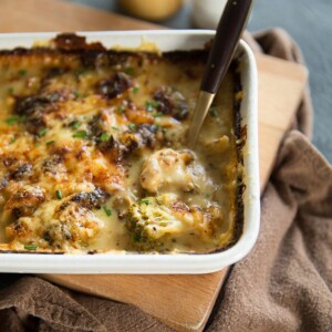 overhead shot of gold spoon digging into broccoli cauliflower cheese bake in white baking dish