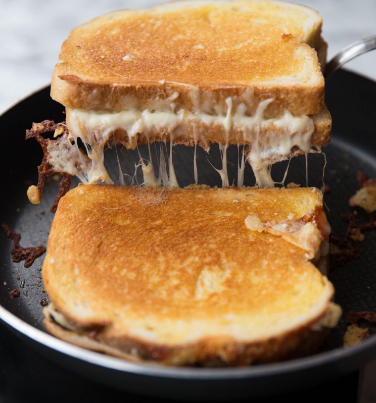 spatula pulling grilled cheese out of pan with cheese pouring out