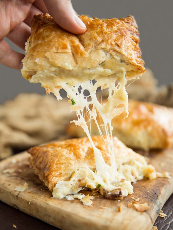 hand pulling half of cheese and onion pasty with cheese dripping out on wooden board