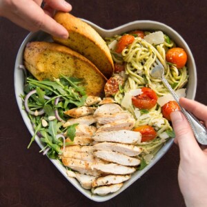 over head shot of pasta served in heart shaped bowls with two hands and forks digging in