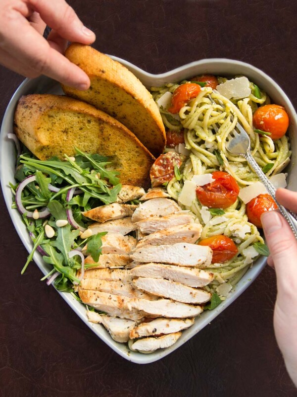 over head shot of pasta served in heart shaped bowls with two hands and forks digging in