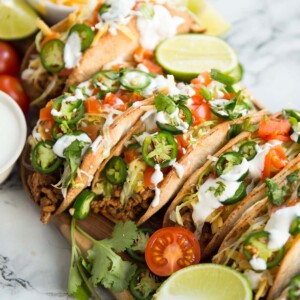 Beef tacos on a wooden board covered in garnishes such as lime, coriander and tomatoes