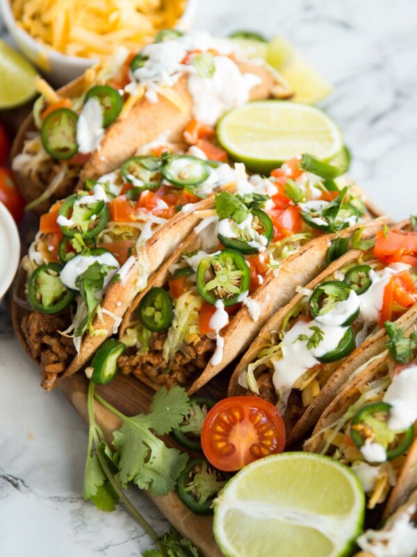 Beef tacos on a wooden board covered in garnishes such as lime, coriander and tomatoes