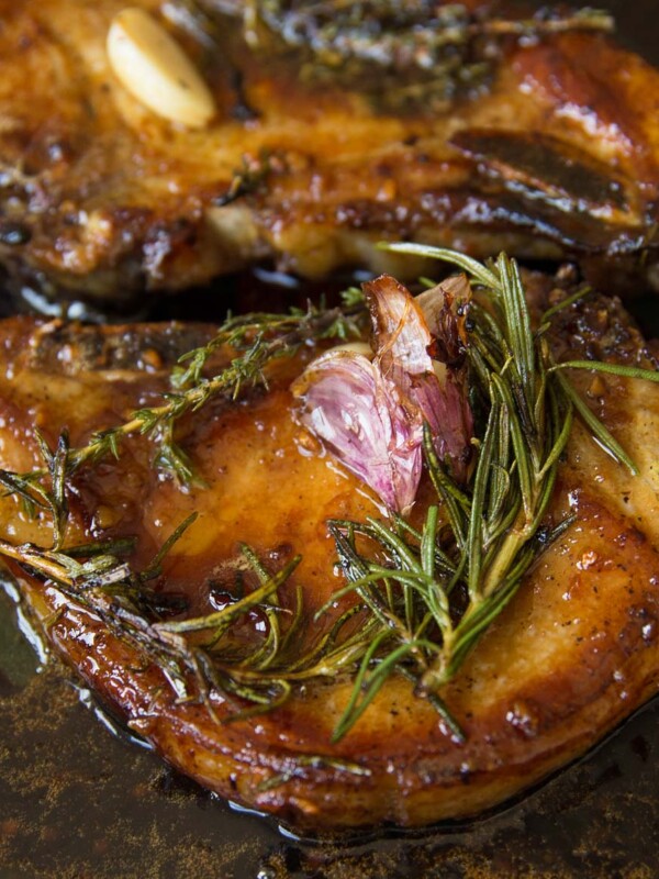 closeup shot of pork chops in skillet garnished with garlic and rosemary