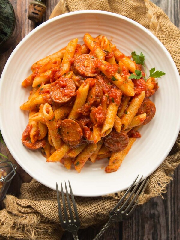 Penne Arrabiata served in a white bowl with two fork on a wooden background