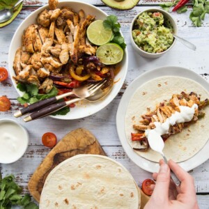 Flat lay of chicken fajitas with sides and garnish including sour cream and guac