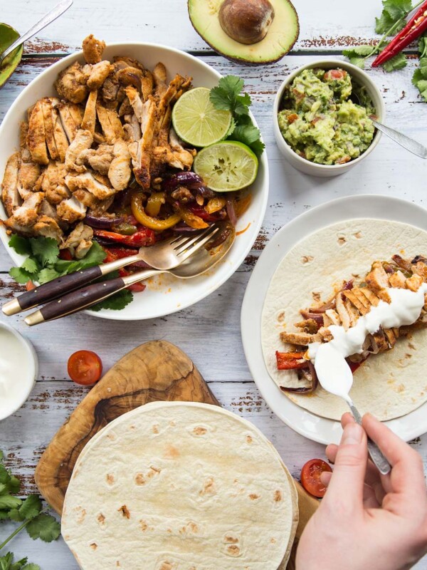 Flat lay of chicken fajitas with sides and garnish including sour cream and guac