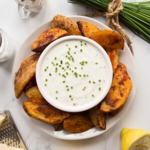 overhead shot of cheese and chive dip on a plate with potato wedges surrounded by garnish