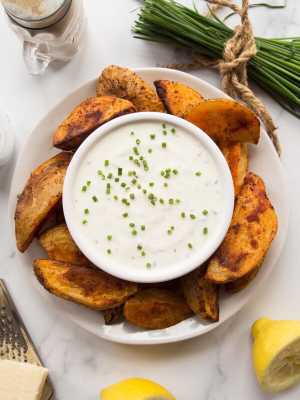 overhead shot of cheese and chive dip on a plate with potato wedges surrounded by garnish