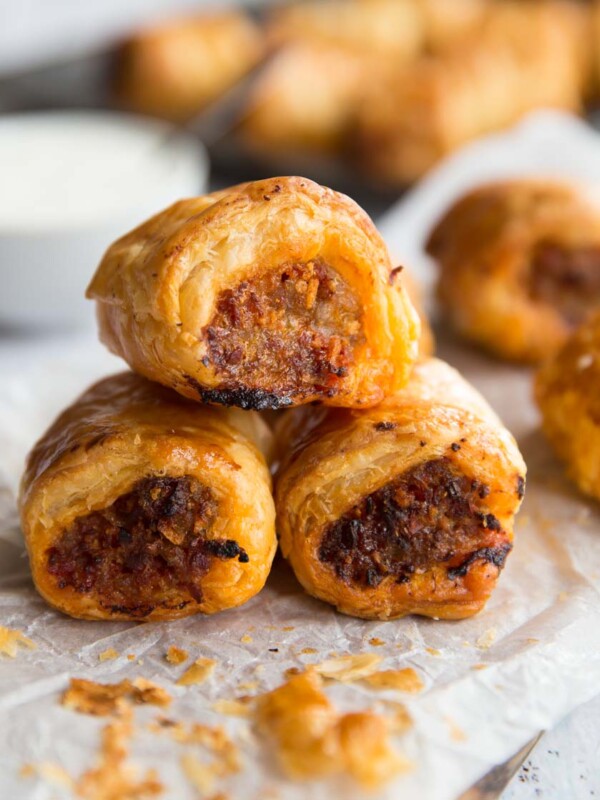 3 Chorizo Sausage Rolls stacked on top of each other with dip and other sausage rolls in the background