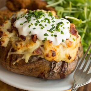 Loaded Potatoes garnished with sour cream and chives with chicken tenders and salad in the background