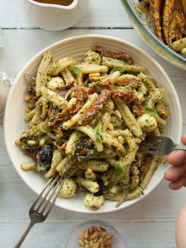 overhead shot of pesto pasta in a white bowl with a hand and fork diving in