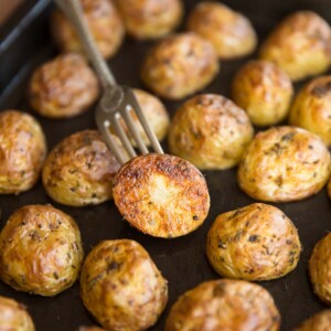 A tray of halved roasted baby potatoes, focus on one with a fork stabbed in