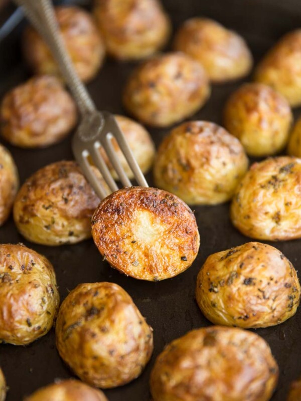 A tray of halved roasted baby potatoes, focus on one with a fork stabbed in