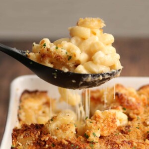 Spoonful of mac and cheese being pulled out of baking dish with cheese dripping down