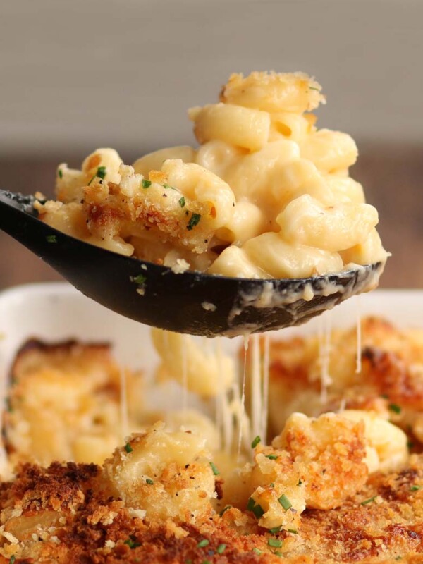 Spoonful of mac and cheese being pulled out of baking dish with cheese dripping down