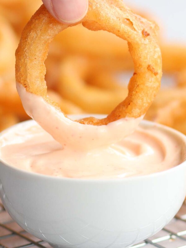 dipping onion ring into srirach mayo with blurred onion rings in the background