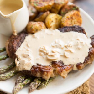 steak on a bed of asparagus with creamy mushroom sauce on top with roast potatoes in the background