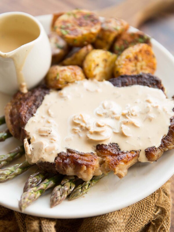 steak on a bed of asparagus with creamy mushroom sauce on top with roast potatoes in the background