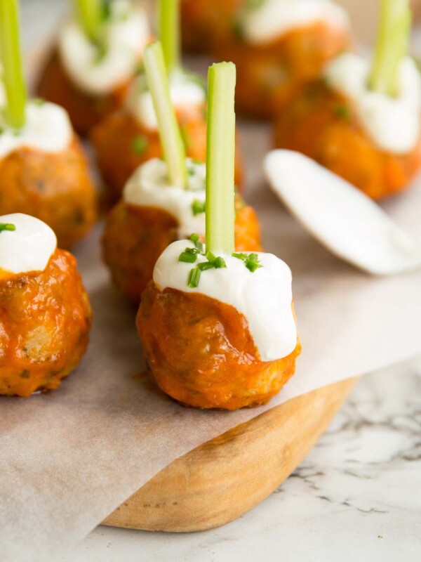 meatballs glazed in buffalo sauce on chopping board with sour cream and chives drizzled on top and celery stuck through the top