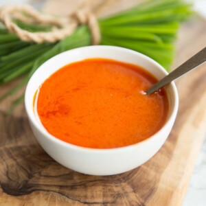 buffalo sauce in a small white pot with spoon in it and chives blurred in the background